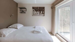 Une chambre d’hôtel avec un grand lit, une fenêtre avec des rideaux, un porte-serviettes fixé au mur et un tableau encadré.
