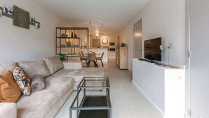 Un salon moderne avec un canapé, une table basse et un téléviseur. Il y a également un coin repas avec des chaises et une table, ainsi qu’une cuisine équipée d’un four à micro-ondes et d’un four traditionnel.