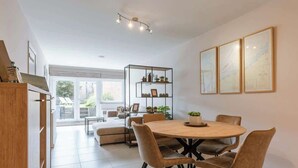Un espace repas moderne avec une table ronde, des chaises rembourrées, une étagère en verre ornée d’objets décoratifs et des œuvres d’art encadrées accrochées au mur.
