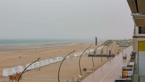 A beach view with a row of white beach huts, a sandy beach, and a clear sky. - Waterfront retreat w/ beach access (De Panne)