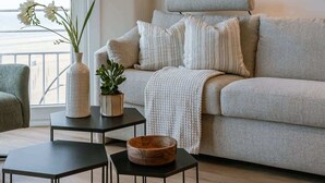 A modern living room with a grey sofa, a small table with a bowl, a vase with flowers, and a wall-mounted light. - Waterfront retreat w/ beach access (De Panne)