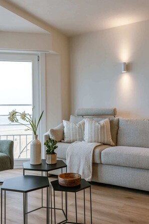 Ein modernes Wohnzimmer mit einem grauen Sofa, einem kleinen Tisch mit einer Schale, einer Vase mit Blumen und einer Wandleuchte.