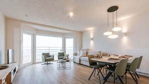A spacious living area with a dining table set for four, a sofa, and a balcony with a view. - Waterfront retreat w/ beach access (De Panne)