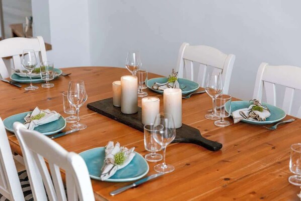 Una mesa de comedor de madera dispuesta con platos verde azulado, copas de vino y velas.