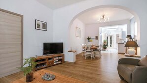 A living room with a TV, wooden coffee table, and a sofa. There is a dining area in the background with a table and chairs.