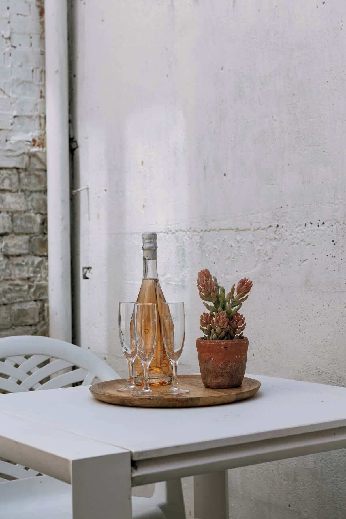 A table with a bottle, glasses, and a potted plant.