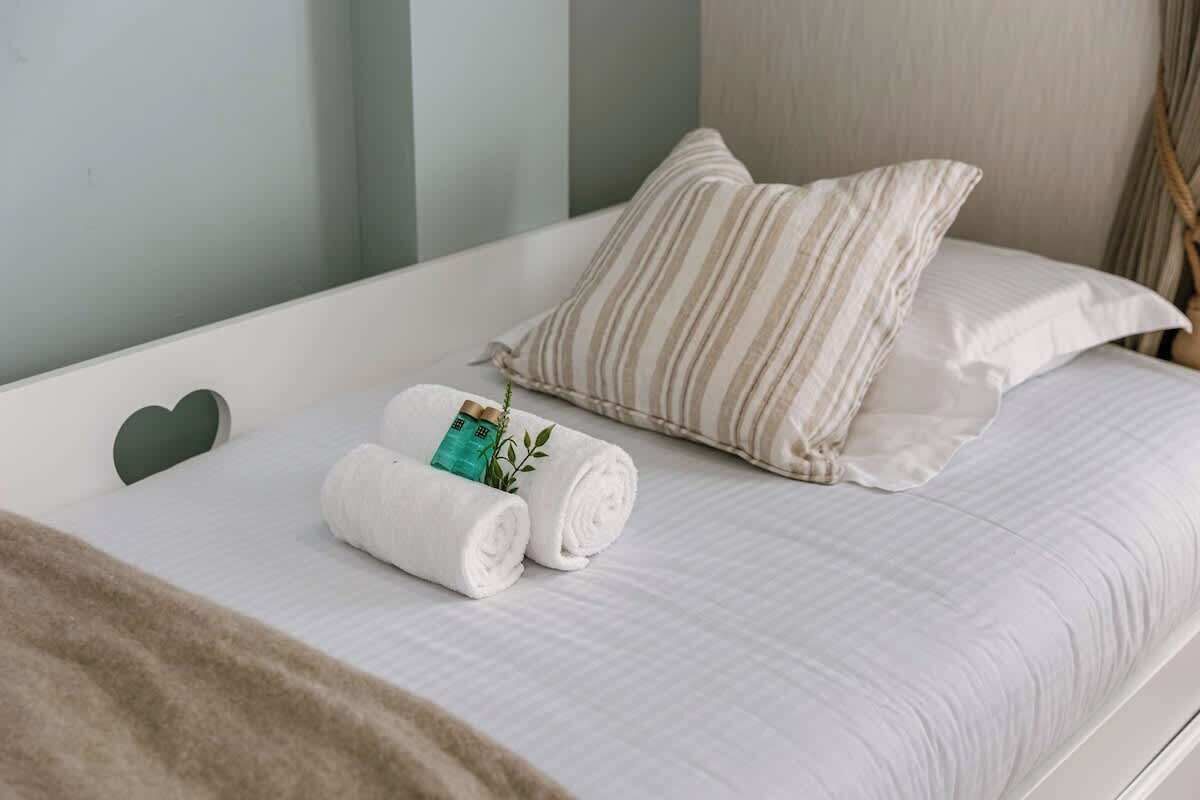 Een net opgemaakt bed met opgerolde witte handdoeken, een gestreept kussen en een hartvormig kussen.