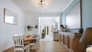 A dining area with a wooden table and chairs, a kitchen with cabinets, and a chandelier.