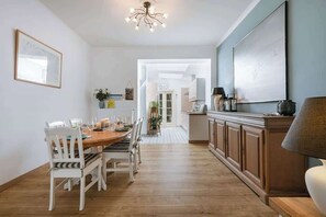 A dining area with a wooden table and chairs, a kitchen with cabinets, and a chandelier.