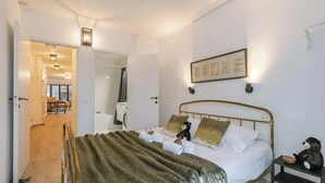 Ein Schlafzimmer mit einem Bett, einem Nachttisch, einem Wandbild und einer Tür zum Badezimmer.