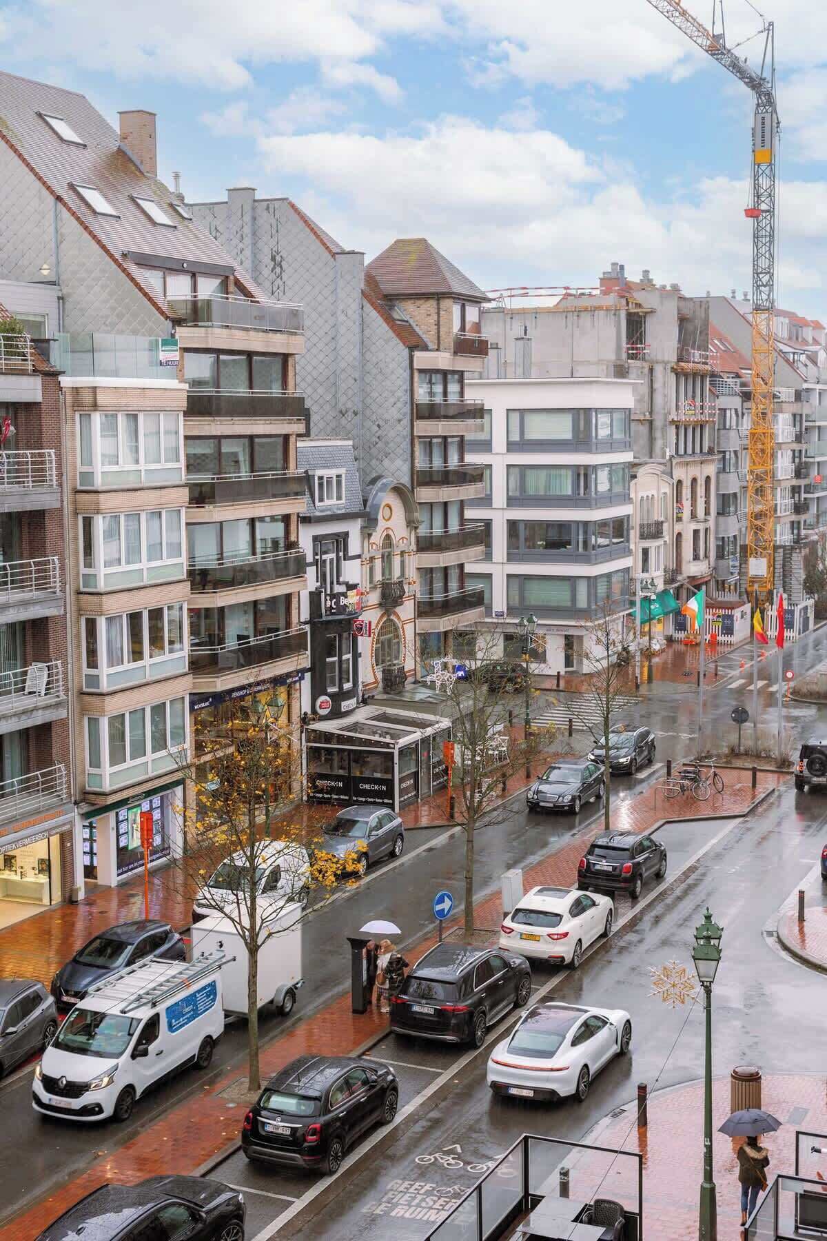 A multi-story urban street with buildings, cars, and a construction crane.