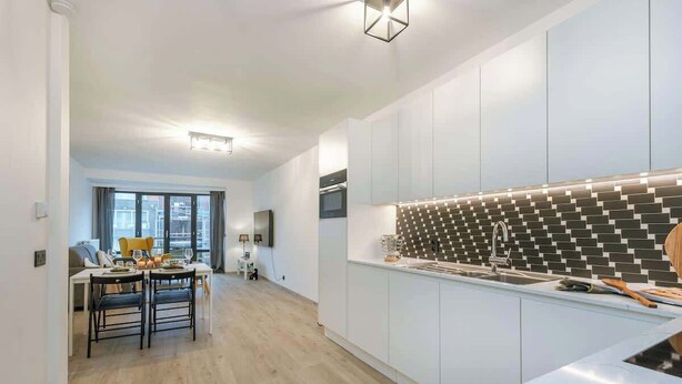 Eine moderne Küche mit weißen Schränken, einer gefliesten Spritzschutzwand und einem Essbereich mit Tisch und Stühlen.