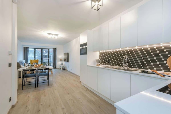Modern kitchen with sleek white cabinetry and a patterned tile backsplash opening to a bright living and dining area.