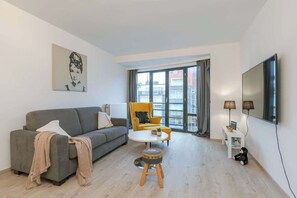 Ein modernes Wohnzimmer mit einem grauen Sofa, einem gelben Sessel, einem kleinen runden Tisch und einem an der Wand montierten Fernseher.