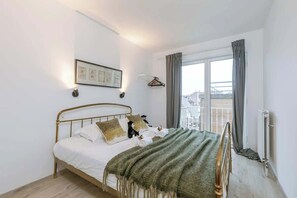Ein ordentlich bezogenes Bett mit einer grünen Decke, ein gerahmtes Bild an der Wand und ein Fenster mit Vorhängen.