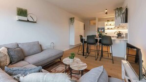 Ein modernes Wohnzimmer mit Sofa, Couchtisch und Essbereich mit Stühlen sowie einer Küche im Hintergrund.