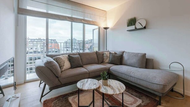 Ein modernes Wohnzimmer mit großem Fenster, einer Couch, einem Couchtisch und einer Wanduhr.