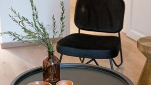 Ein kleiner runder Tisch mit einer Kerze, einer Holtschale und einer Vase mit Grünpflanzen.