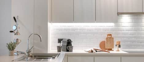 A modern kitchen with a stainless steel sink, a coffee maker, and a wooden cutting board on the countertop.