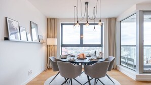 Ein Essbereich mit einem runden Tisch, Stühlen, einer Chandelüster und einem großen Fenster mit Blick auf die Stadt.
