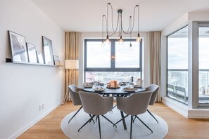 Ein Essbereich mit einem runden Tisch, Stühlen, einer Chandelüster und einem großen Fenster mit Blick auf die Stadt.