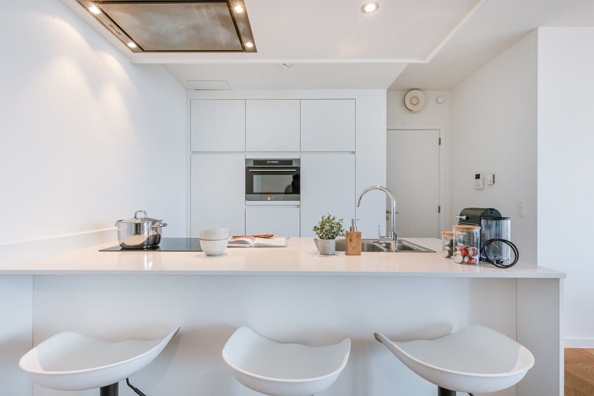 A modern kitchen with white cabinetry, a central island with bar stools, a built-in oven, and a sink.