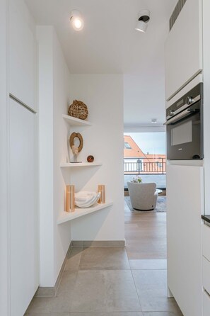 Eine moderne Küche mit weißen Schränken, einem eingebauten Ofen und Blick auf einen Balkon mit roten Ziegeln.
