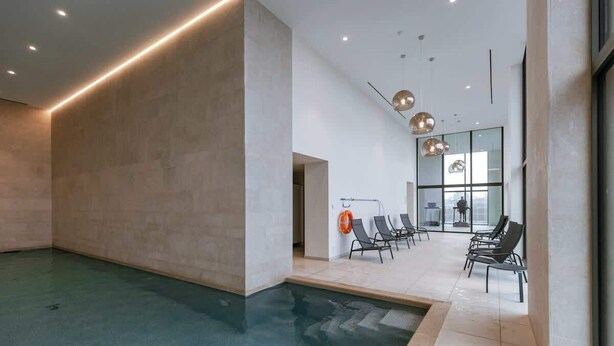 A modern indoor swimming pool with a concrete wall, lounge chairs, and pendant lighting. - Beachside apartment w/ pool & gym access (Oostende)