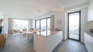 A modern kitchen with a central island, large windows, and a dining area with chairs. - Beachside apartment w/ pool & gym access (Oostende)