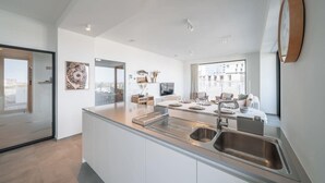 A modern kitchen with a central island, stainless steel sink, and a large window providing a view of the city. - Beachside apartment w/ pool & gym access (Oostende)