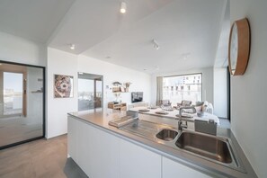 A modern kitchen with a central island, stainless steel sink, and a large window providing a view of the city. - Beachside apartment w/ pool & gym access (Oostende)