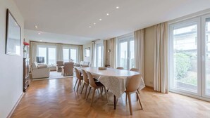 A spacious dining area with a large table, multiple chairs, and large windows offering a view of the outdoors. - 4-bedroom escape w/ backyard & beach access (Knokke-Heist)