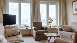 A living room with a TV, two sofas, a chair, a small table, and a window with curtains. - 4-bedroom escape w/ backyard & beach access (Knokke-Heist)