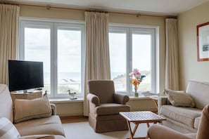 A living room with a TV, two sofas, a chair, a small table, and a window with curtains. - 4-bedroom escape w/ backyard & beach access (Knokke-Heist)