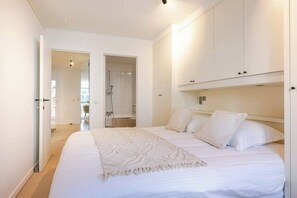 A bedroom with a bed, white walls, a door leading to a bathroom, and a wardrobe. - Beachside Apartment w/ Private Parking & Balcony (Oostende)