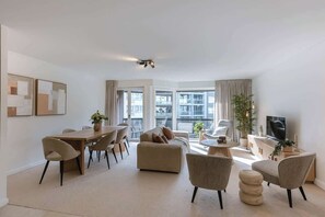 Un salon moderne comprenant un coin repas, un canapé, un téléviseur et de grandes fenêtres.