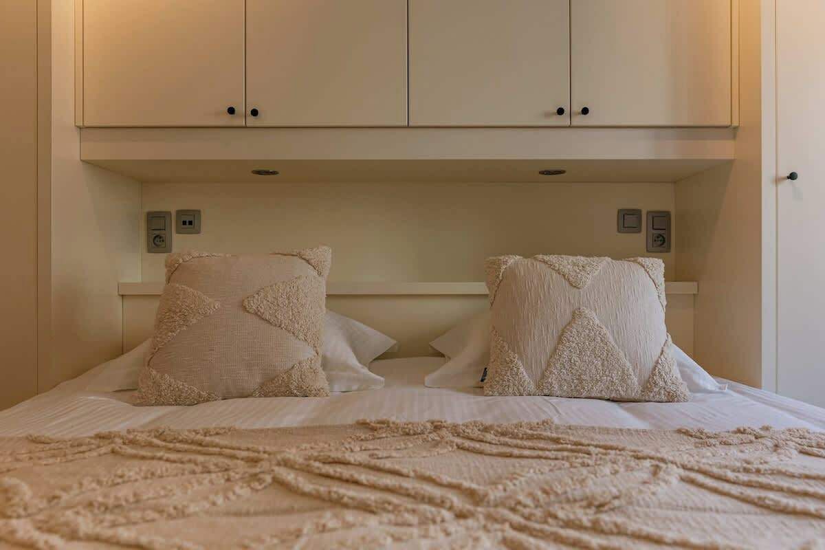 Ein Bett mit einer gemusterten Decke, zwei Kissen mit geometrischem Muster und einem weißen Kopfteil.
