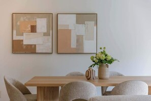 A dining area with a wooden table, four chairs, two abstract paintings, and a vase with flowers. - Beachside Apartment w/ Private Parking & Balcony (Oostende)