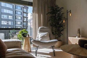 A modern living room with a large window, a comfortable armchair, a potted plant, and a floor lamp. - Beachside Apartment w/ Private Parking & Balcony (Oostende)