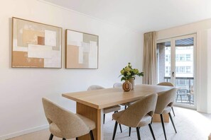 Un espace repas moderne avec une table en bois et six chaises, un vase de fleurs et deux tableaux abstraits accrochés au mur.