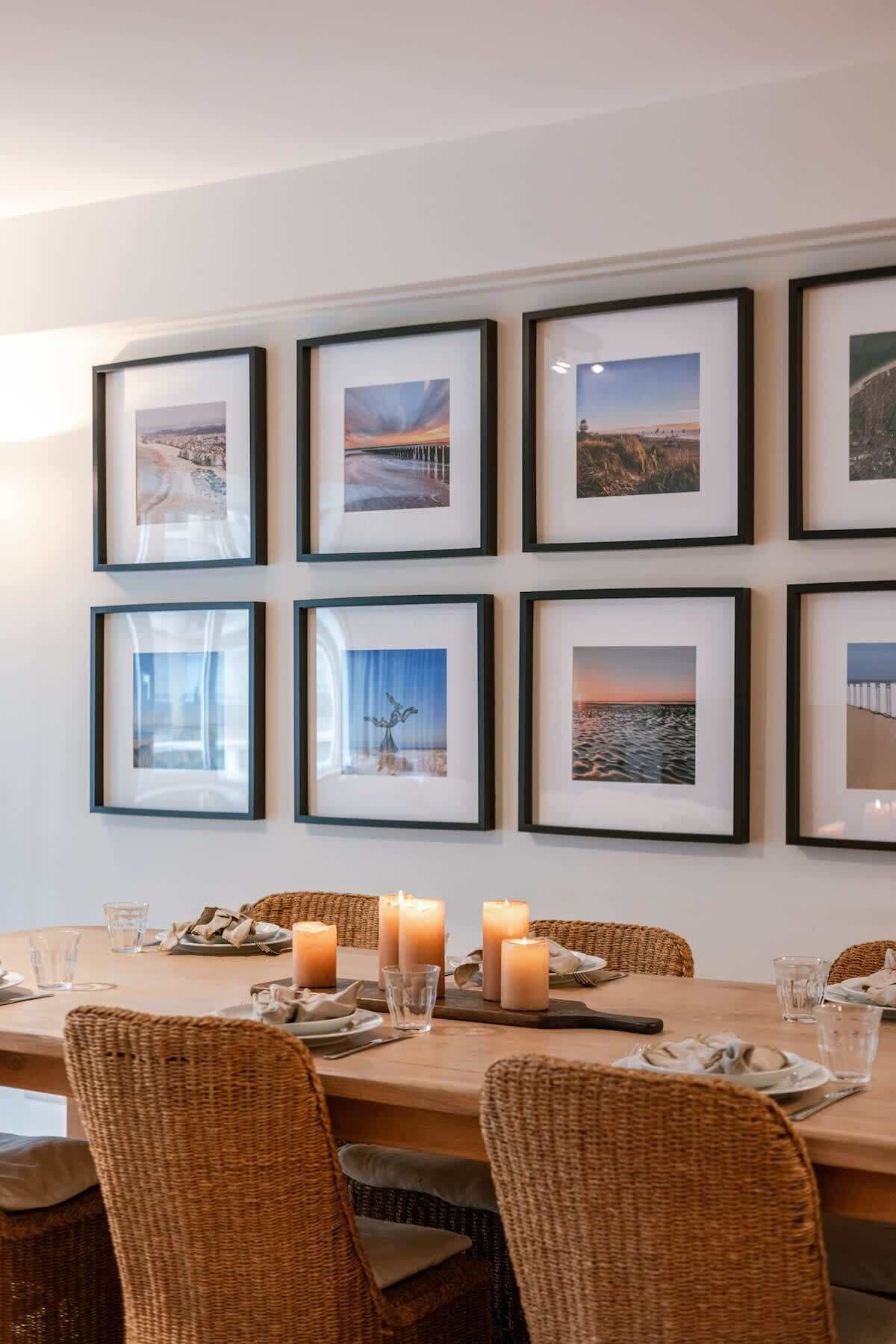 Een eetgedeelte met een lange tafel, rieten stoelen en ingelijste foto's aan de muur.