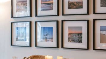 Een eetgedeelte met een lange tafel, rieten stoelen en ingelijste foto's aan de muur.