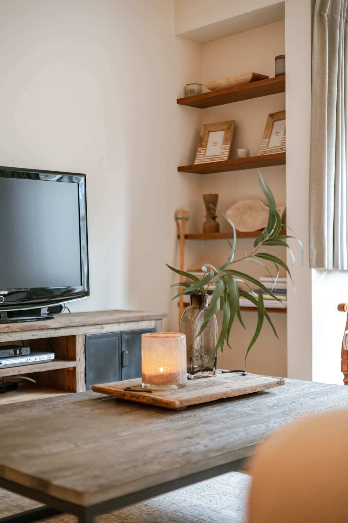 Een woonkamer met een televisie, houten planken, een plant en een kaars op een houten tafel.