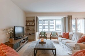 A living room with a TV, sofa, coffee table, and a window with curtains. - Beach-access apt w/ terrace & city skyline views (Knokke-Heist)