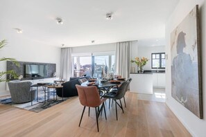 Ett modernt vardagsrum med en matplats, en tv och ett stort fönster med utsikt över staden.