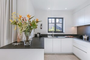 A modern kitchen with white cabinets, a black countertop, and a window with a view. - Bright 2BR apt near coastal tram w/ terrace (Knokke-Heist)