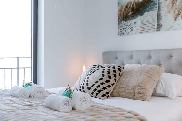 Cozy bedroom with textured pillows and neatly rolled towels on a soft beige blanket.