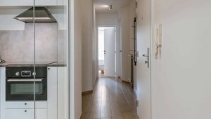 Una cocina moderna con horno integrado y un panel de vidrio, un pasillo con suelo de madera y una puerta que da a otra habitación.