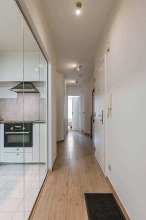 A modern kitchen with a built-in oven and a glass partition, a hallway with wooden flooring, and a door leading to another room. - Cozy 2BR unit w/ kitchen & TV (Knokke-Heist)