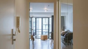 Un pasillo que conduce a una sala de estar con un separador de vidrio, suelo de madera y una puerta con un teléfono.